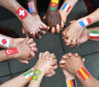 Photo of a circle of joined hands; different flags painted on each wrist