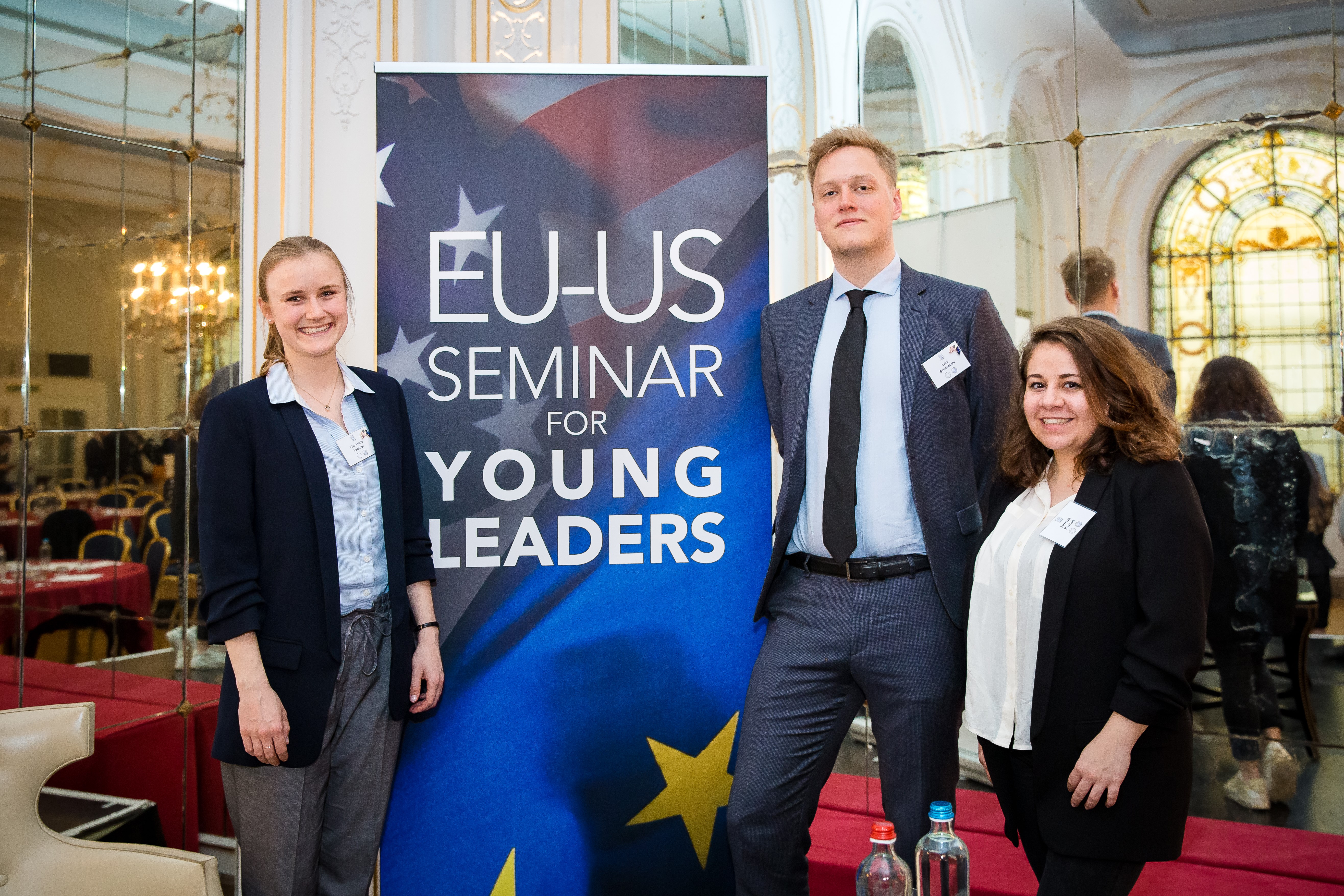 Lisa Lechner, Lars Svensmark and Miriam Karout stand in front of a pull up banner that says: EU-US Seminar for Young Leaders